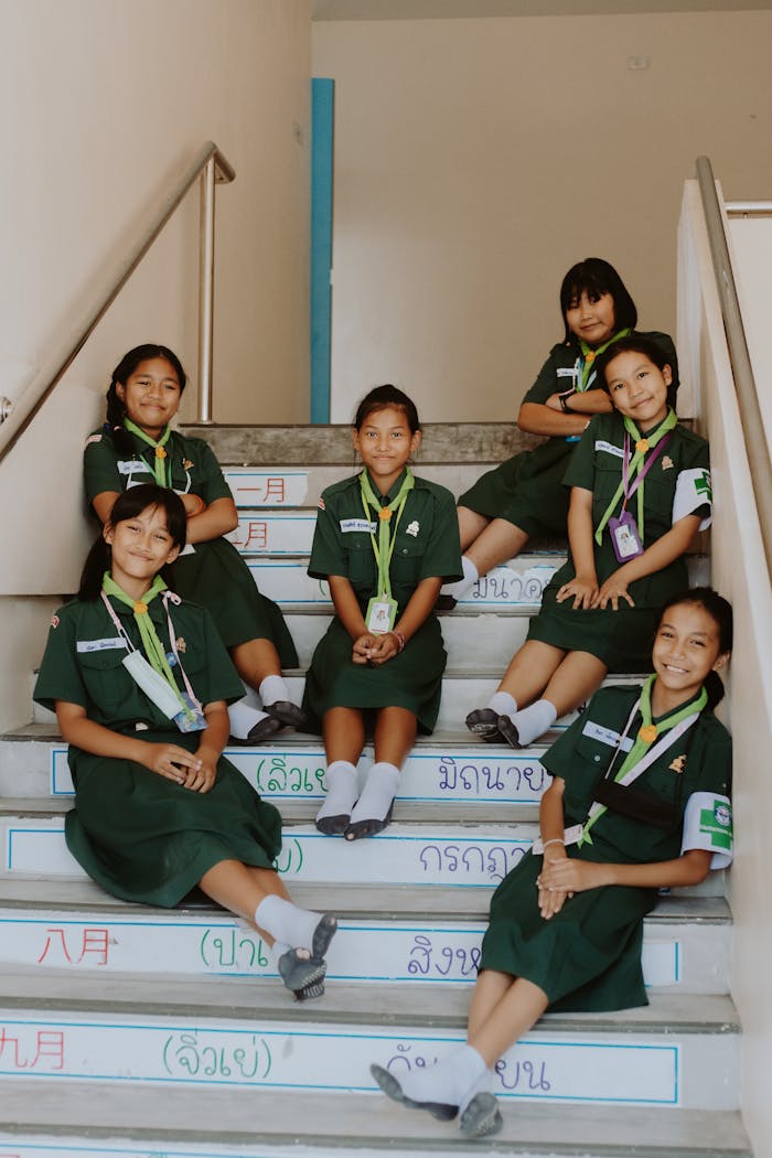 Group of six school girls in uniform sitting on stairs, smiling at camera.